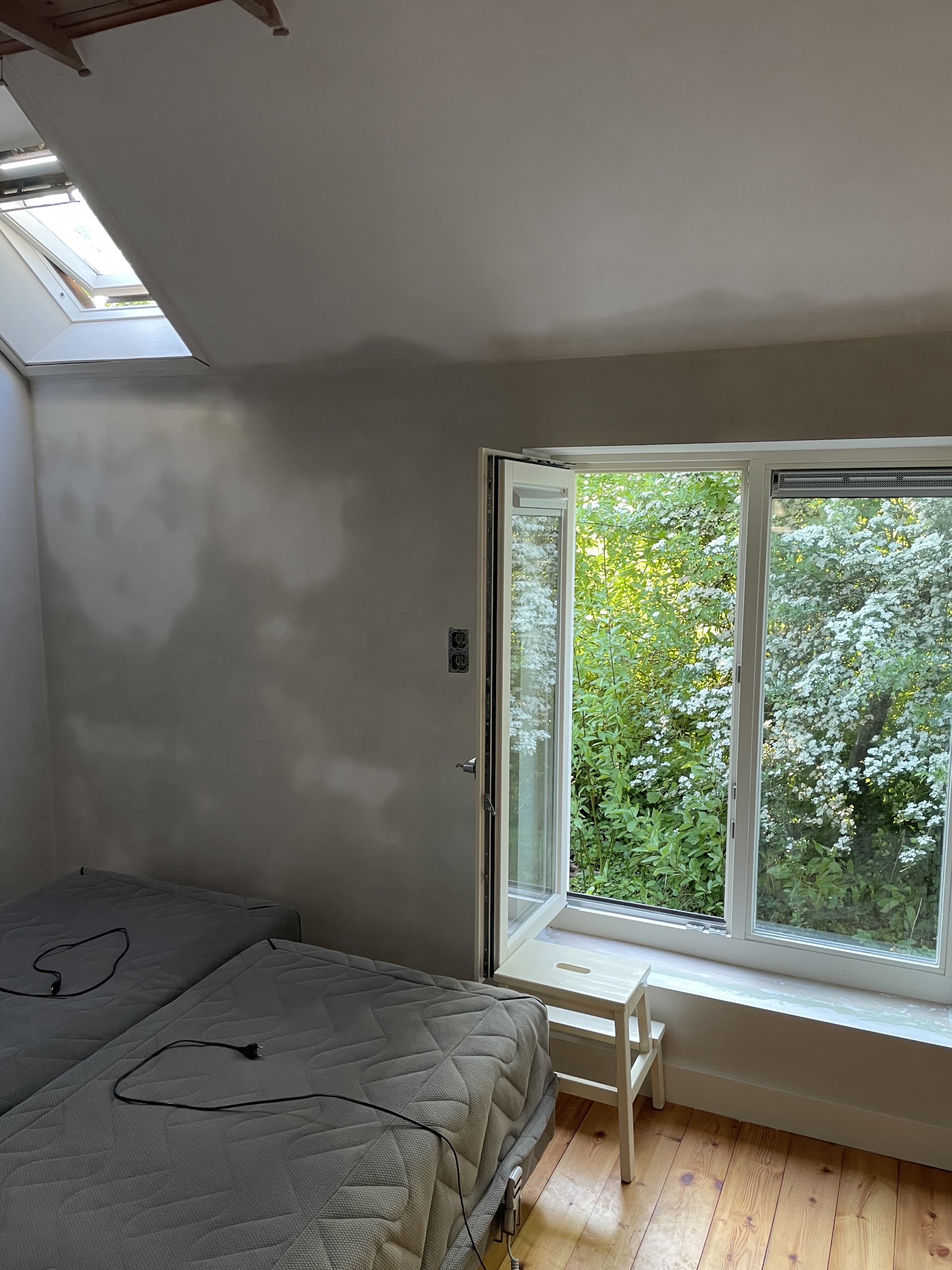 Zolderslaapkamer met vers stucwerk dat nog droogt, raam open naar de tuin